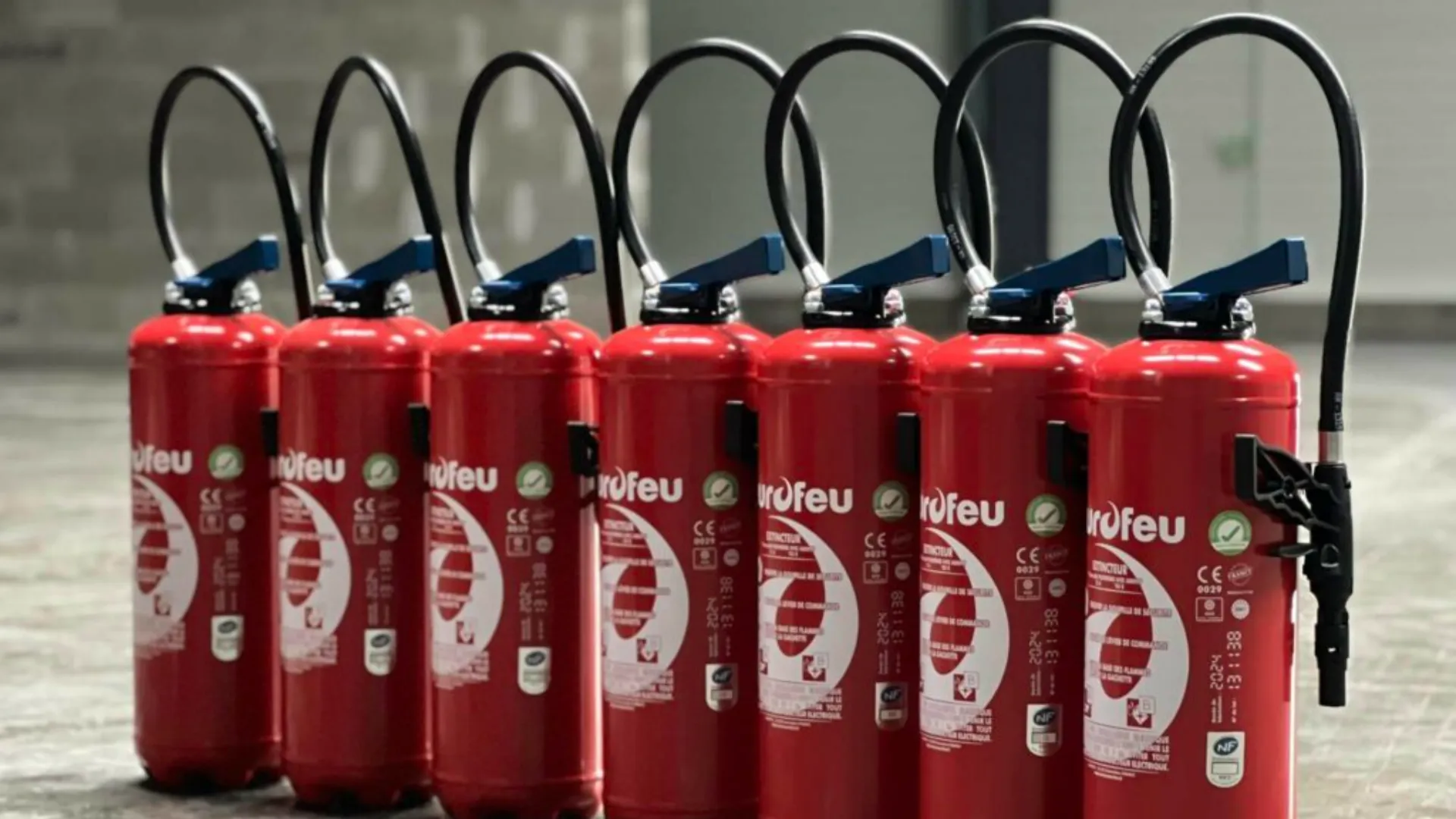 Sept extincteurs à poudre rouge alignés avec buses bleues et anses de transport, équipements de sécurité incendie professionnels conformes aux normes CE, essentiels pour la sécurité en Vendée