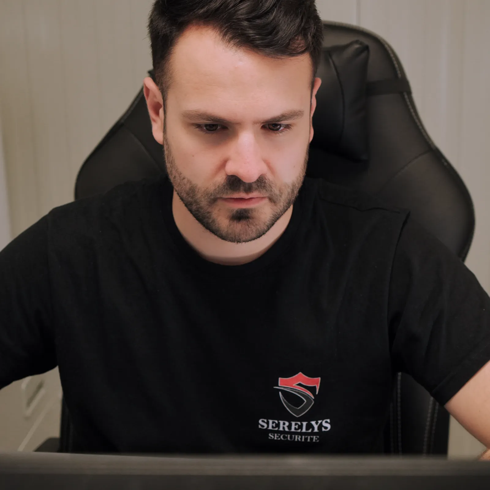 Technicien SERELYS SÉCURITÉ en Vendée concentré sur un écran de surveillance, portant le polo noir de l'entreprise avec logo