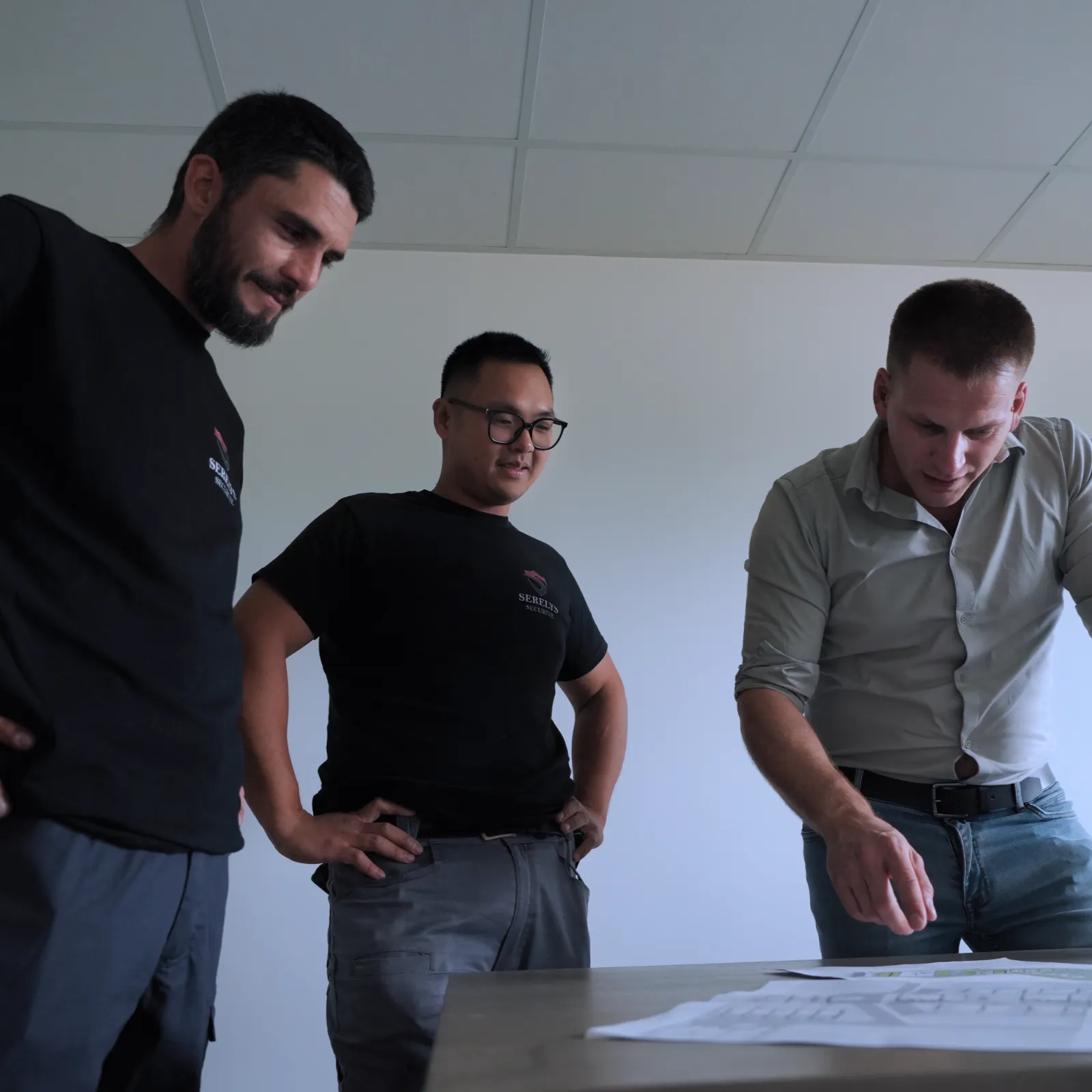 Trois professionnels de SERELYS SÉCURITÉ en Vendée examinent des plans de sécurité intrusion et alarme sur mesure pour un projet premium en réunion technique