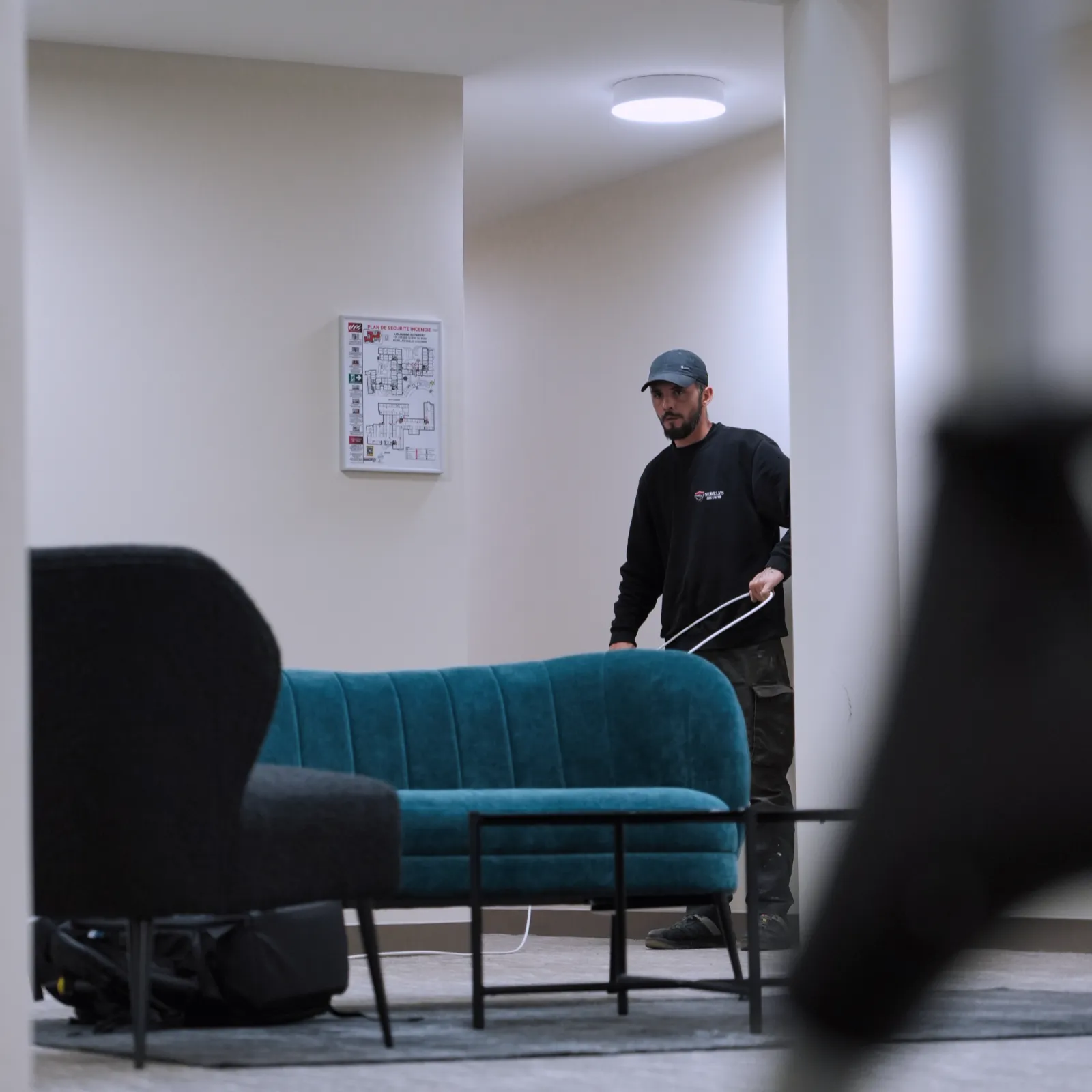 Technicien SERELYS SÉCURITÉ en Vendée installant un système de vidéosurveillance dans un espace professionnel moderne avec canapé bleu et schéma technique mural