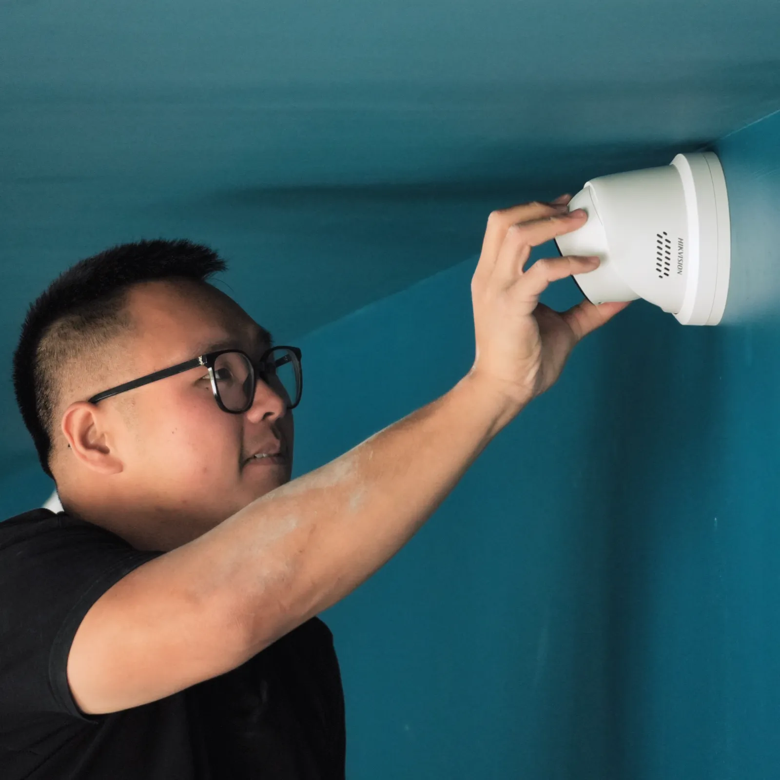 Technicien SERELYS SÉCURITÉ en Vendée installant un détecteur de fumée blanc au plafond, démontrant l'expertise en solutions de sécurité et vidéosurveillance