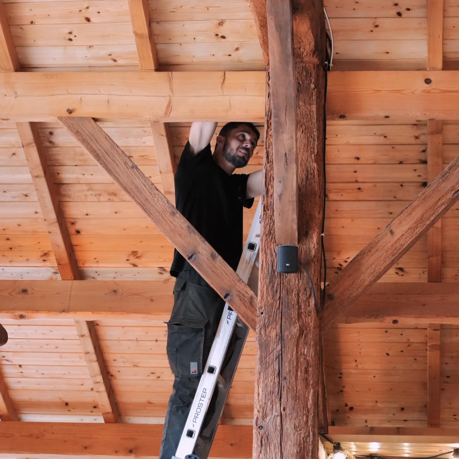 Technicien SERELYS SÉCURITÉ en Vendée installant une caméra de vidéosurveillance dans les combles d'une structure bois, équipé d'un niveau et d'outils professionnels