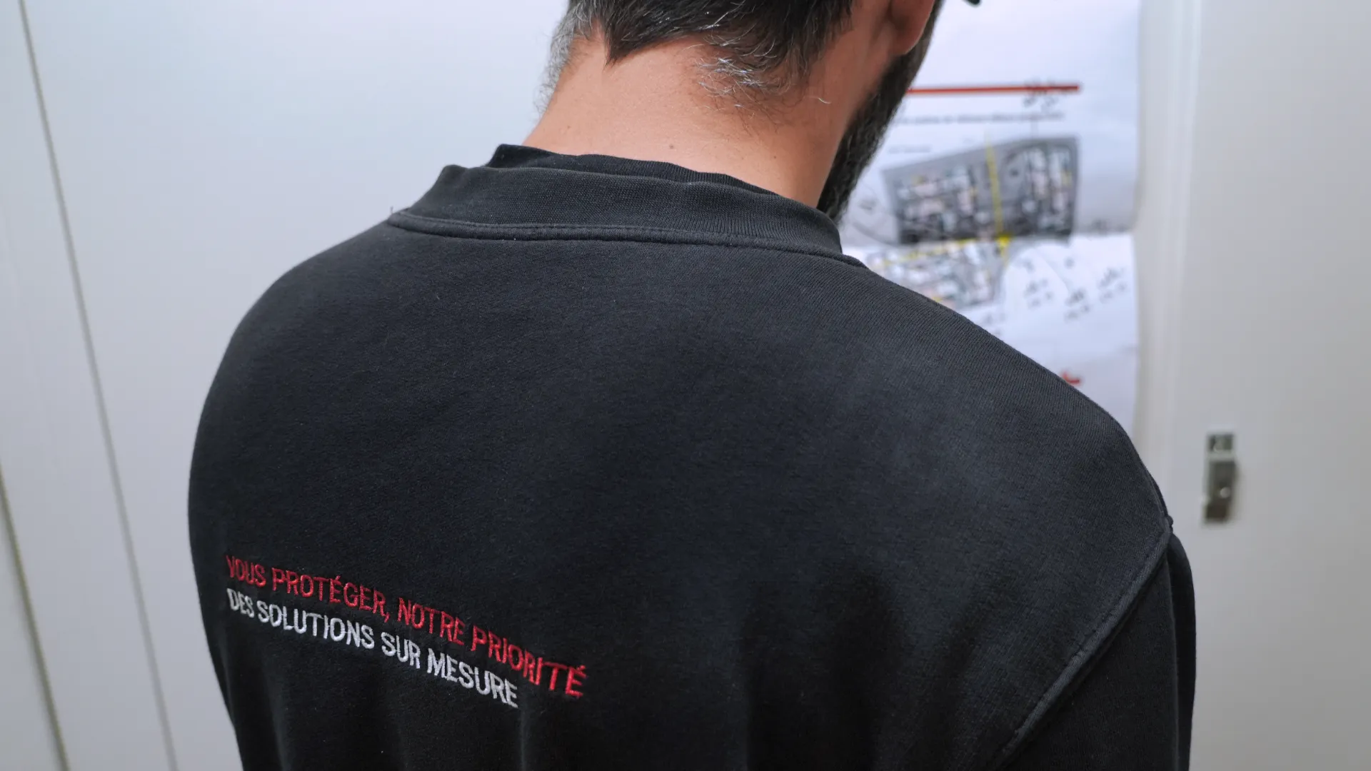 Technicien SERELYS SÉCURITÉ en Vendée portant un polo noir avec message de protection, consultant des plans de vidéosurveillance et solutions de sécurité