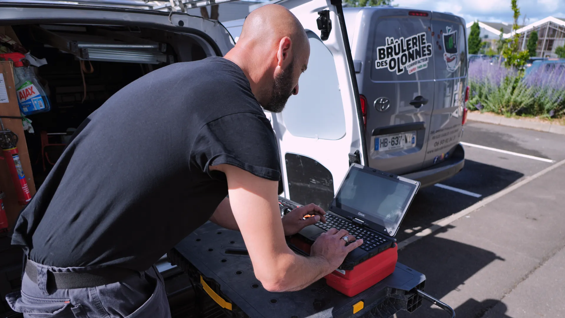 Technicien SERELYS SÉCURITÉ en Vendée effectuant une installation ou maintenance de système de vidéosurveillance depuis un véhicule équipé, utilisant un ordinateur portable pour configurer les solutions de sécurité