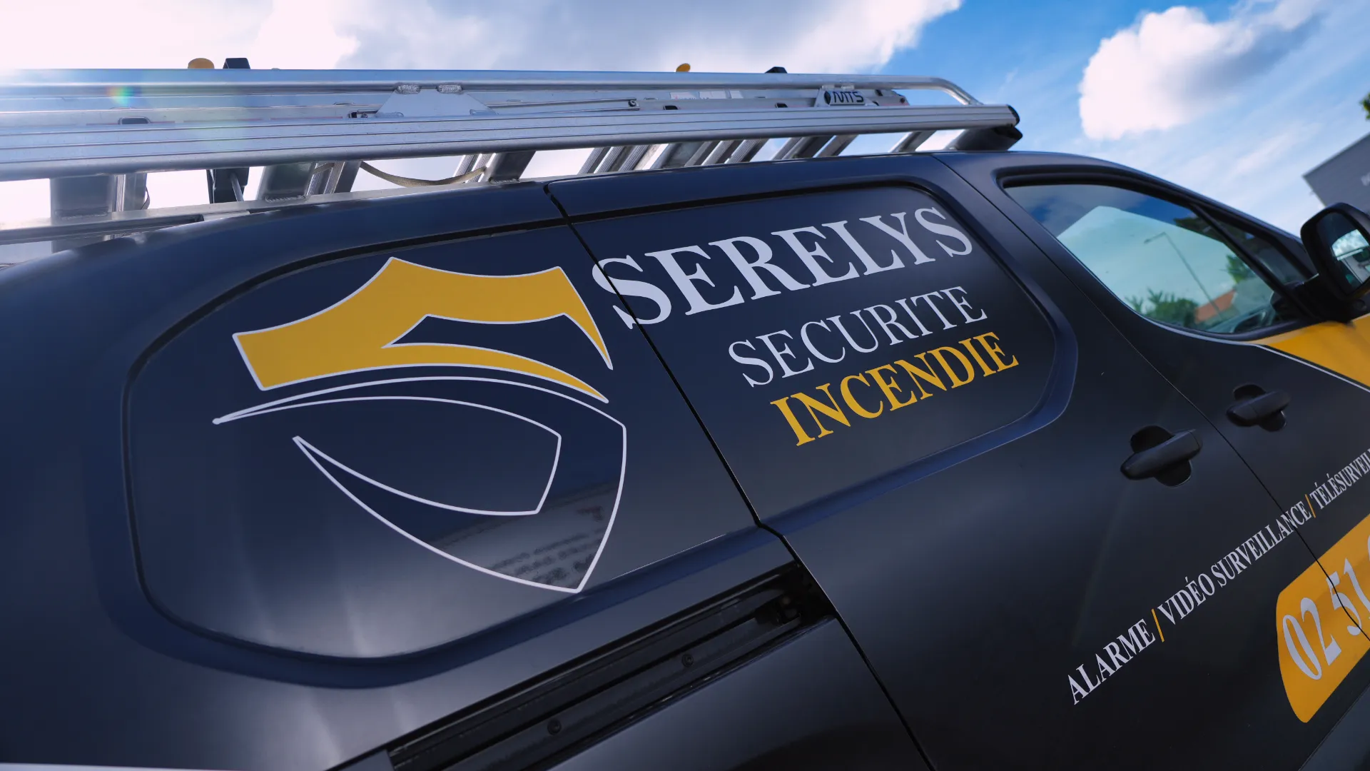 Véhicule de service SERELYS SÉCURITÉ en Vendée avec logo bouclier, inscriptions vidéosurveillance et alarme incendie sur carrosserie bleu marine et jaune