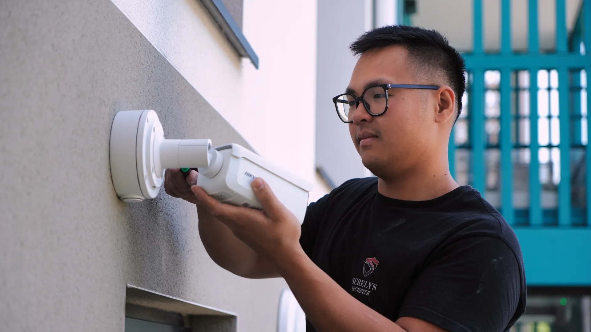 Technicien SERELYS SÉCURITÉ en Vendée installant une caméra de vidéosurveillance sur un mur extérieur, équipé d'outils professionnels