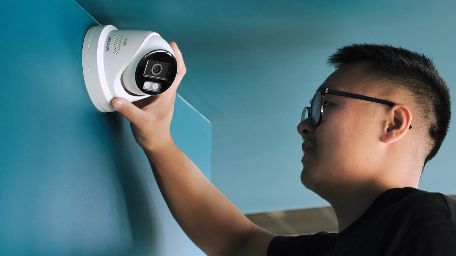 Technicien SERELYS SÉCURITÉ en Vendée installer une caméra de surveillance dome blanche haute définition sur mur bleu, équipé de lunettes de protection