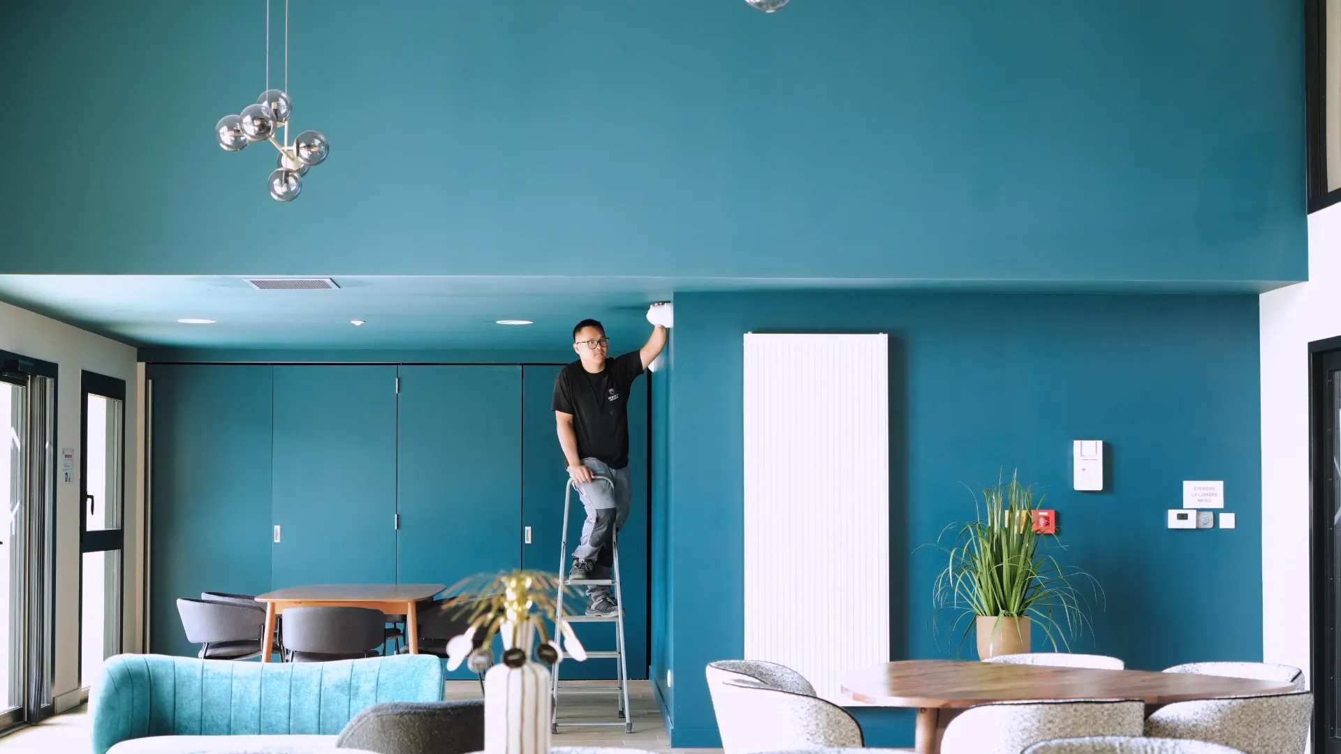 Technicien SERELYS SÉCURITÉ en Vendée installant un système de vidéosurveillance au plafond d'un bureaux moderne aux murs turquoise