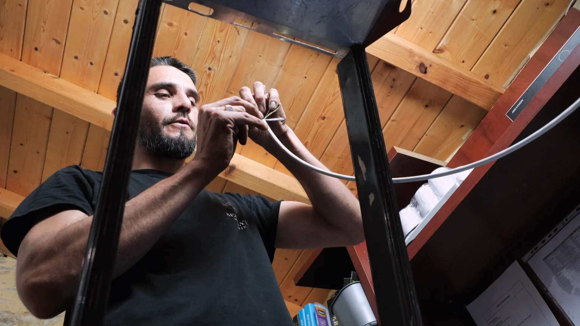 Technicien SERELYS SÉCURITÉ en Vendée installant un câble de vidéosurveillance sous plafond en bois, démontrant l'expertise en solutions de sécurité professionnelles