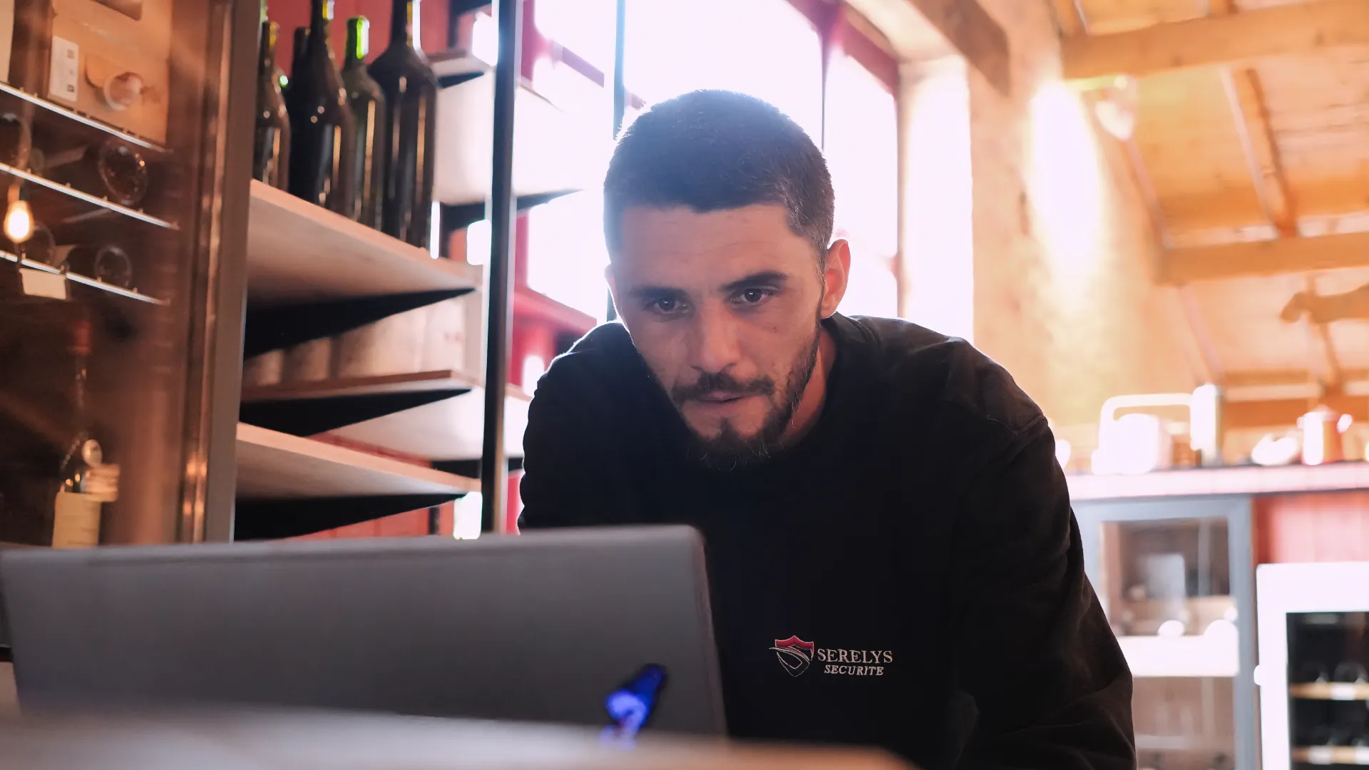 Technicien SERELYS SÉCURITÉ en Vendée consultant un laptop pour configurer une solution de vidéosurveillance, dans un showroom moderne avec équipements de sécurité