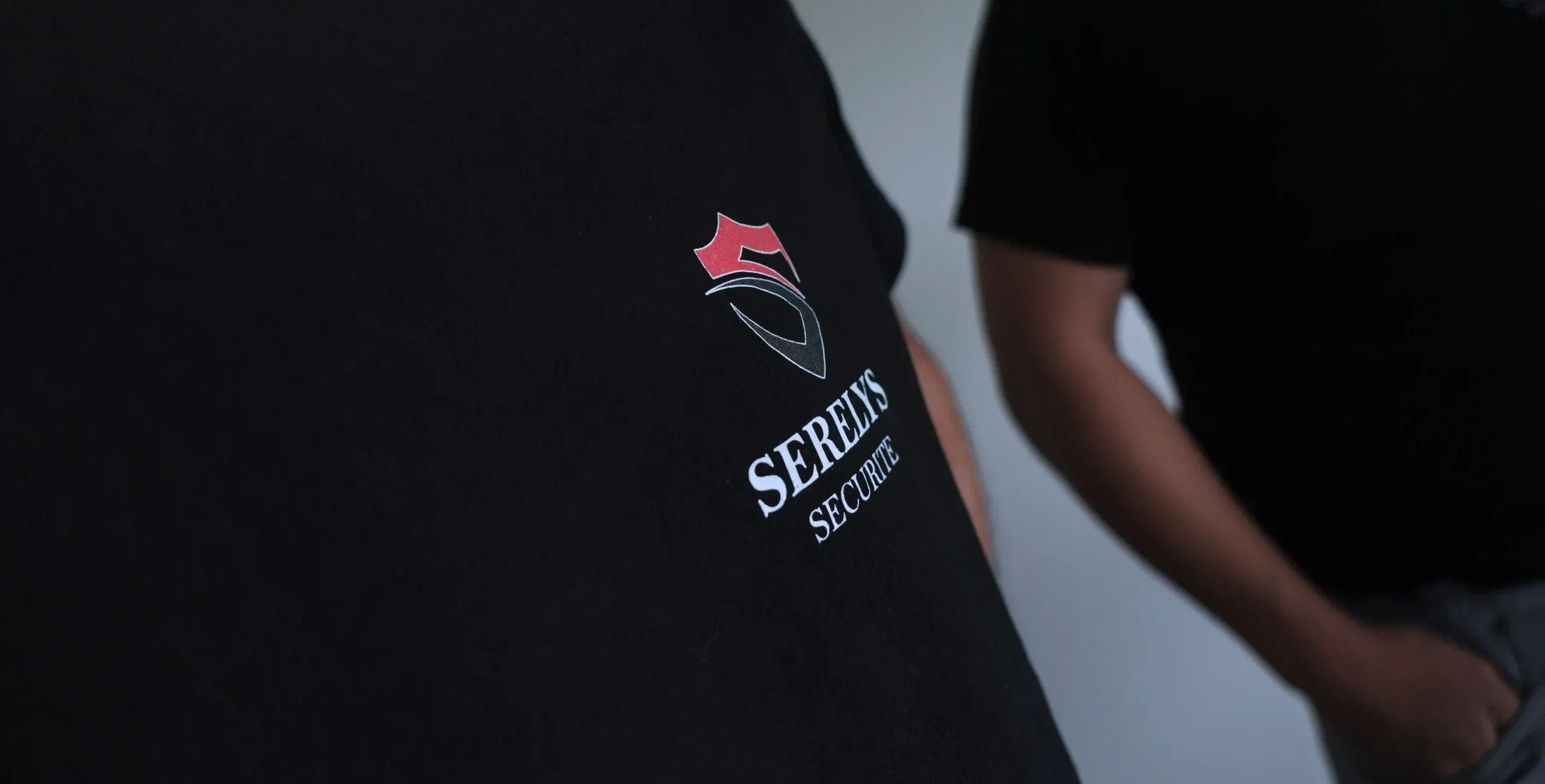 Logo SERELYS SÉCURITÉ avec symbole de shield rouge et bleu sur vêtement noir, entreprise spécialisée en sécurité intrusion et alarme sur mesure en Vendée