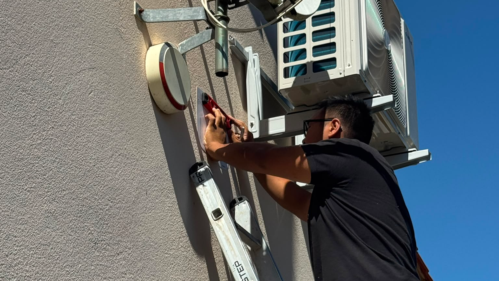 Technicien SERELYS SÉCURITÉ en Vendée effectuant l'installation d'une caméra de vidéosurveillance sur façade avec climatiseur visible